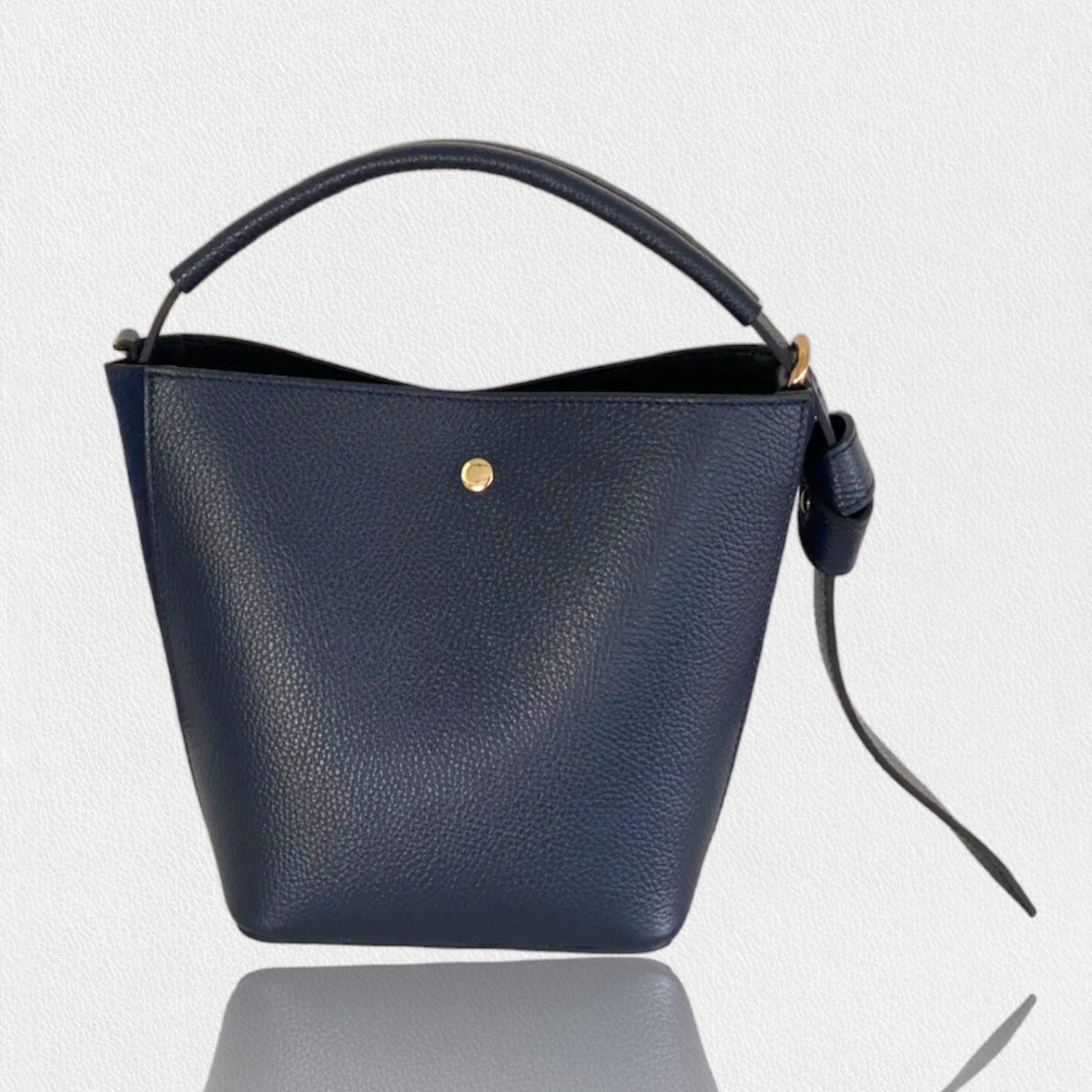 Introducing the SMALL LEATHER BUCKET HANDBAG by LE BORSETTE: This sleek white handbag boasts a structured design with a single top handle and detachable crossbody straps. With its minimalistic style and tiny gold accent on the front, its clean lines and smooth texture provide a modern, sophisticated look.