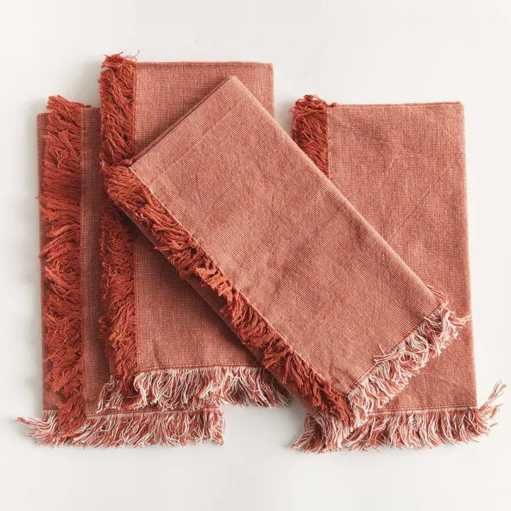 Four NAPA HOME AND GARDEN - AURA DINNER NAPKINS in rust, made of washable cotton with fringed edges, are neatly fanned out on a white surface.
