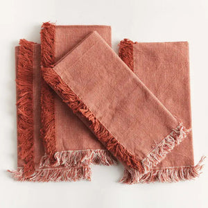 Four NAPA HOME AND GARDEN - AURA DINNER NAPKINS in rust, made of washable cotton with fringed edges, are neatly fanned out on a white surface.