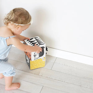 The WEE GALLERY - JUNGLE SOFT BLOCK by WEE GALLERY is a soft fabric cube perfect for stimulating a baby's developing senses. It features monochrome patterns and playful designs, including a cute monkey illustration on one side and a yellow leaf on another. Inspired by jungle life and animals, this toy boasts various textures and small loops on top for easy grasping.
