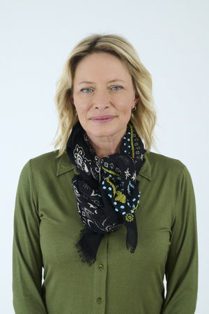 The STORIATIPIC - NELLY Wool Bandana Scarf with Embroidery in Black features a sophisticated paisley and floral design in shades of blue, green, and white. Delicately finished with small frayed edges and shown folded in a loose loop against a white background, this elegant accessory captures the essence of French designer flair, expertly crafted by STORIATIPIC to elevate any ensemble.