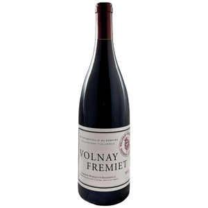 A bottle of MARQUIS D’ANGERVILLE VOLNAY 1ER CRU ‘FREMIET’ 2017 with a white label sits next to a glass of red wine on a white table.