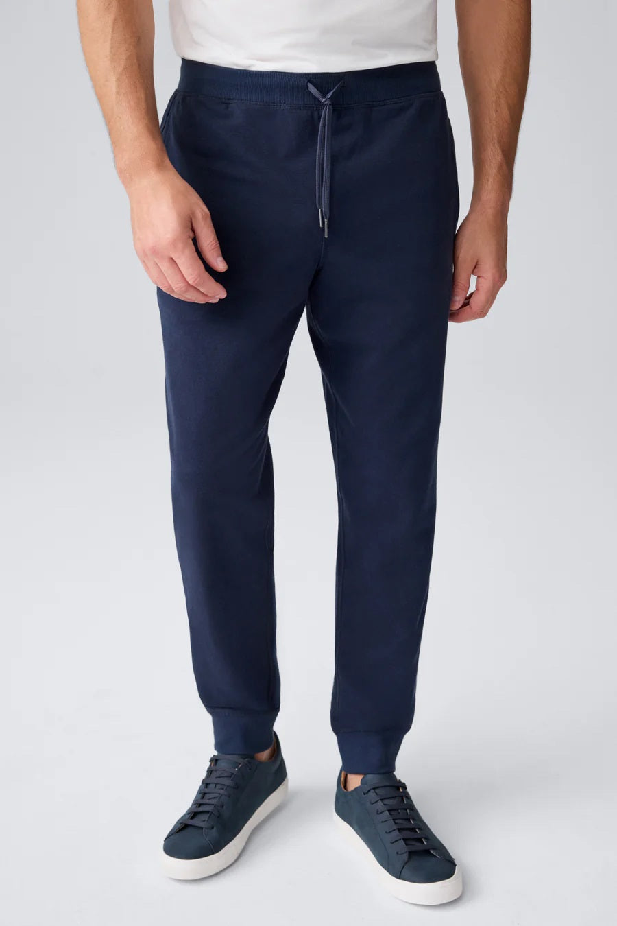 A person wears MACK WELDON ACE Relaxed Fit Sweatpants in True Navy - Bird’s Eye, styled with pockets and matching navy sneakers, against a plain light gray background. Only the lower body is visible.