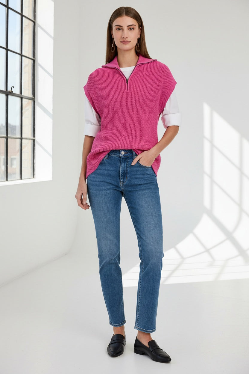 A woman with straight brown hair wears the HINSON WU BROOKE Sleeveless Knit Vest in bright pink over a white shirt and blue jeans, standing against a plain light background.