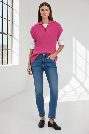 A woman with straight brown hair wears the HINSON WU BROOKE Sleeveless Knit Vest in bright pink over a white shirt and blue jeans, standing against a plain light background.