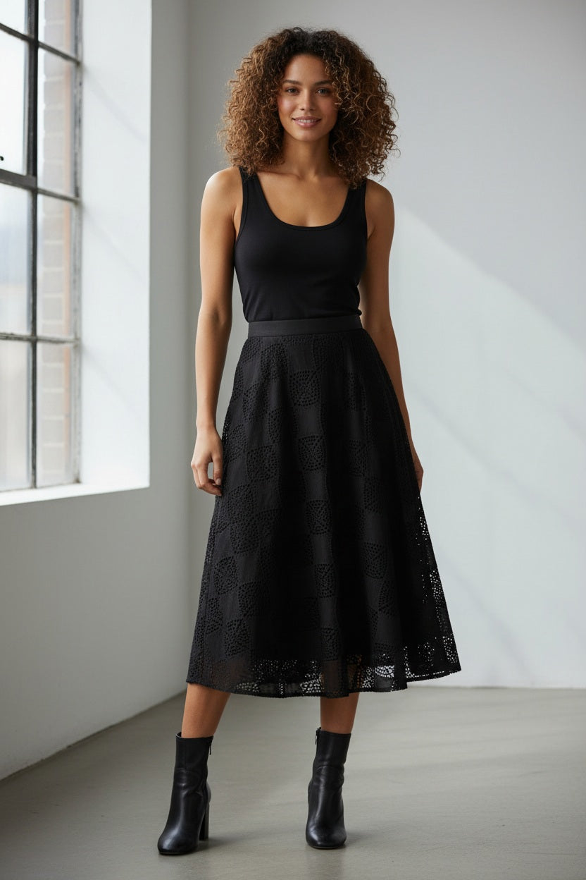 The SFIZIO - PATCHWORK CROCHET SUEDE CIRCLE SKIRT by SFIZIO is a black A-line midi skirt that features a checkered pattern with alternating solid and crochet knit squares, offering a modern look. The hemline falls slightly below the knee, adding an elegant touch to this patchwork design. Made in Italy.