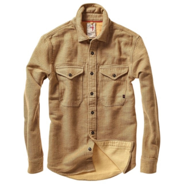 Dressed in the RELWEN Utility Workshirt in cornmeal herringbone layered over a blue and white striped shirt and paired with green pants, the individual stands with relaxed hands by their sides, capturing the effortless sophistication of luxury workwear. The person’s head is partially out of frame.