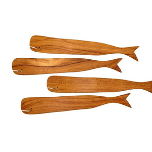 The BE HOME - TEAK WHALE SPREADERS by BE HOME, INC rest on a round white marble cutting board with a hole at the top, displayed on a wooden surface.