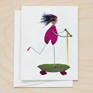 The PETAL PEOPLE PRESS - SCOOT birthday card by PETAL PEOPLE PRESS features a charming figure made from leaves and petals riding a plant-based scooter, ideal for nature lovers. Card is shown on a white surface with leaves, scissors, and paperclips.