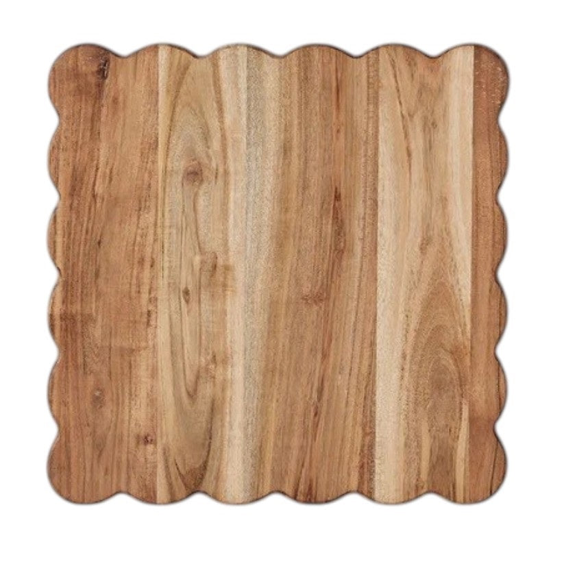 The ETUHOME Natural Square Scalloped Cutting Board, Medium, crafted from durable acacia wood, stands upright against a light gray wall on a white marble surface.