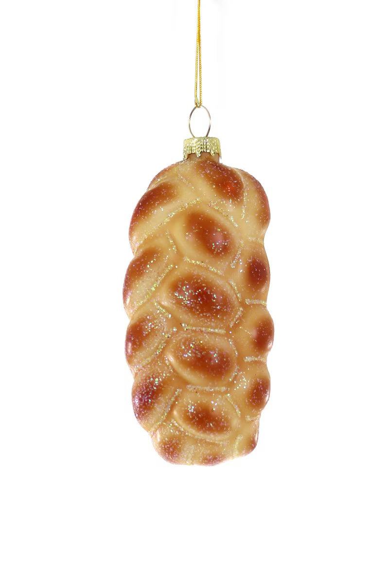 Introducing the CHALLAH BREAD ORNAMENT by CODY FOSTER: a stunning glass Christmas tree decoration designed to resemble a beautifully braided loaf of bread. Complete with a golden string at the top, this ornament captures the authentic texture and color of real baked bread. Its charming dimensions are enhanced by a dusting of glitter, adding a festive sparkle to your holiday décor.