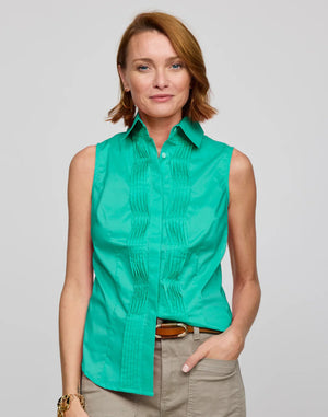 A person with short red hair smiles in a tailored HINSON WU Lilith Sleeveless Shirt featuring decorative pleats, paired with a brown belt and khaki pants against a plain light gray background.