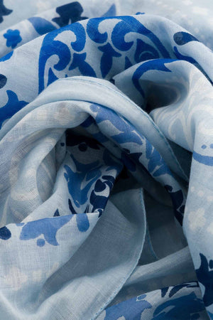 The MAISON LECOMTE - DINARD BANDANA SCARF IN COTTON VOILE by MAISON LECOMTE FLAMENT is a square, light blue cotton voile bandana adorned with an intricate paisley and floral pattern in shades of dark and light blue, elegantly displayed flat on a white background—an ideal accessory for any occasion.
