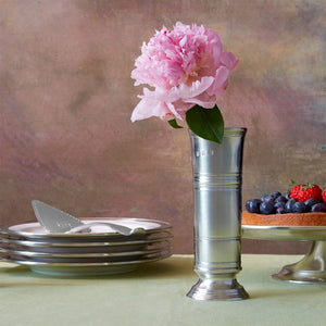 The MATCH Footed Cylinder Pewter Vase by MATCH displays a bouquet of pink, peach, and yellow ranunculus against a white background—an elegant and timeless hostess gift.