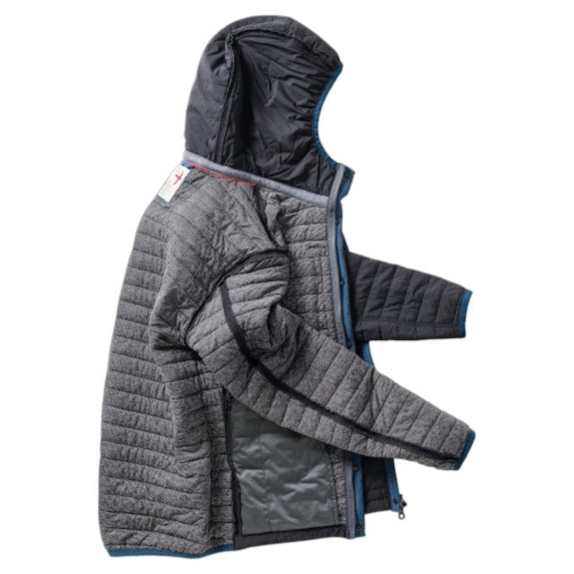 Wearing the RELWEN - WINDZIP HOOD IN BLACK FADE, a black water-resistant jacket with recycled polyester insulation from RELWEN, a person stands on a snowy path in blue pants, covering their face with their hand. Snow falls gently as snow-laden trees fill the background.