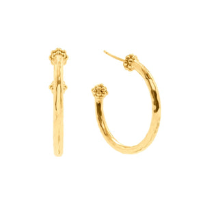A woman with curly hair wears CAPUCINE DE WULF’s Berry Slice Hoop Earrings—a pair of hammered gold hoops—along with a chunky gold chain necklace. With her eyes closed and a serene expression, she poses against a softly blurred background, showcasing her appreciation for handmade jewelry.