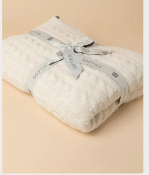 Folded off-white SOFTIES - CABLE KNIT MARSHMALLOW BLANKET tied with a branded ribbon.
