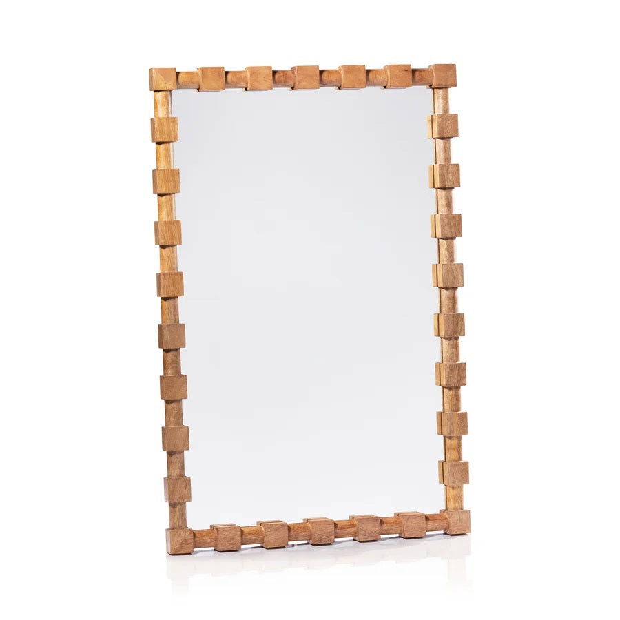 The ZODAX CADIER MANGO WOOD WALL MIRROR with a rectangular frame hangs on a textured gray wall above a wooden table displaying a potted plant, framed photo, books, and decor.