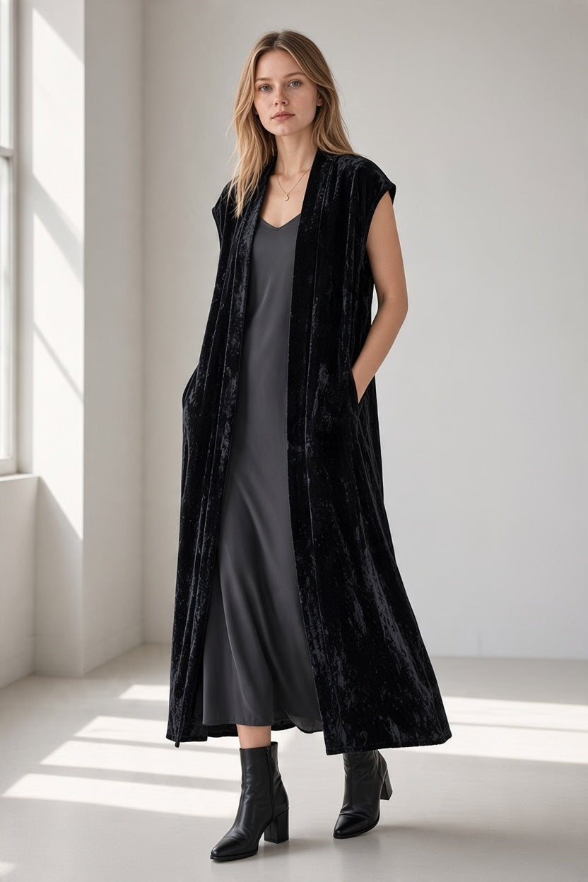 A woman wearing a GAYNOR BONGARD - POETA VELVET GILET IN BLACK over a dark gray midi dress and black ankle boots.