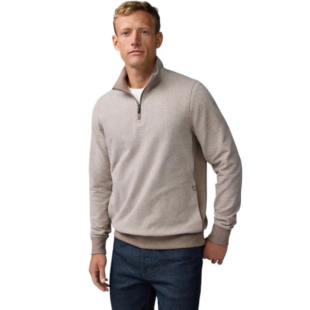 A man with short light brown hair stands in profile, wearing the MACK WELDON Ace 1/2 Zip Sweater in Herringbone and dark pants, one hand in his pocket, against a plain light gray background.