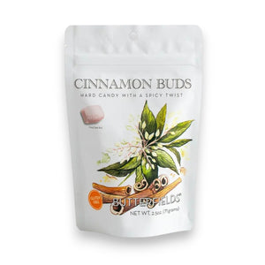 A white pouch of BUTTERFIELDS - CINNAMON BUDS hard candy by BUTTERFIELDS features an illustration of cinnamon sticks and leaves, capturing the inviting warmth of holiday spices. The packaging includes a gluten free label, a small image of the candy, and lists a net weight of 2.5 oz (71g).