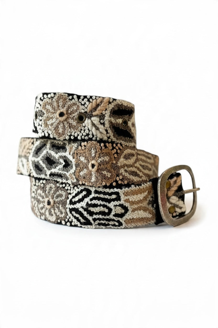 A woman wears a cream-colored knit sleeveless dress cinched with a JENNY KRAUSS - MONOCHROMATIC EMBROIDERED WOOL BELT IN BLACK featuring floral embroidery and a metal buckle.