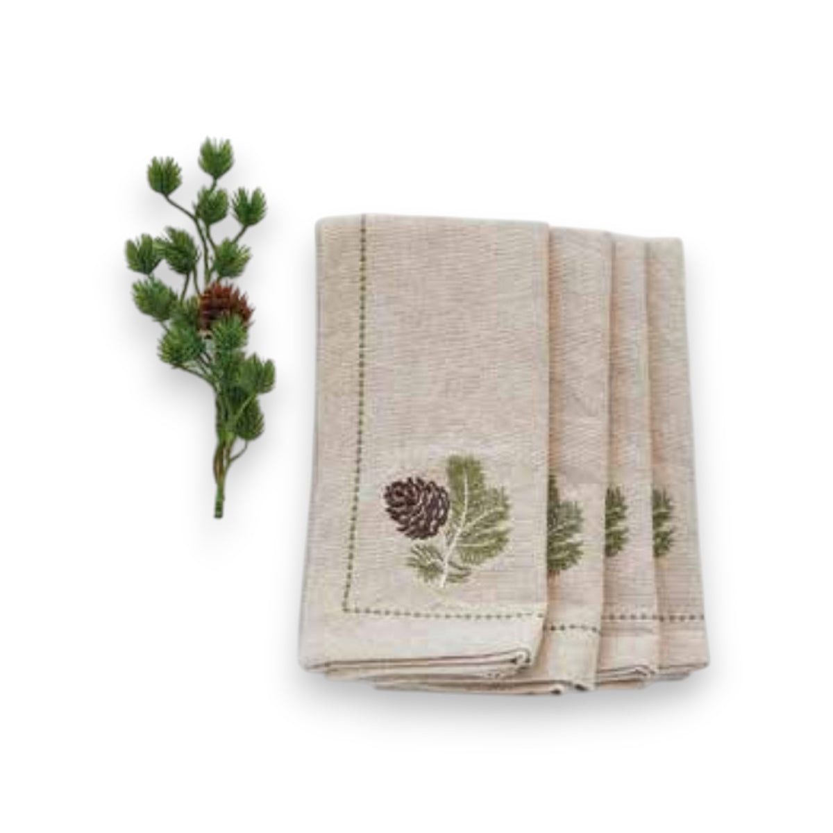 Four beige cotton NAPKIN WITH METALLIC THREAD EMBROIDERED BORDER by CREATIVE COOP, featuring embroidered pinecones and green leaves, are shown beside a pinecone branch on a white background.