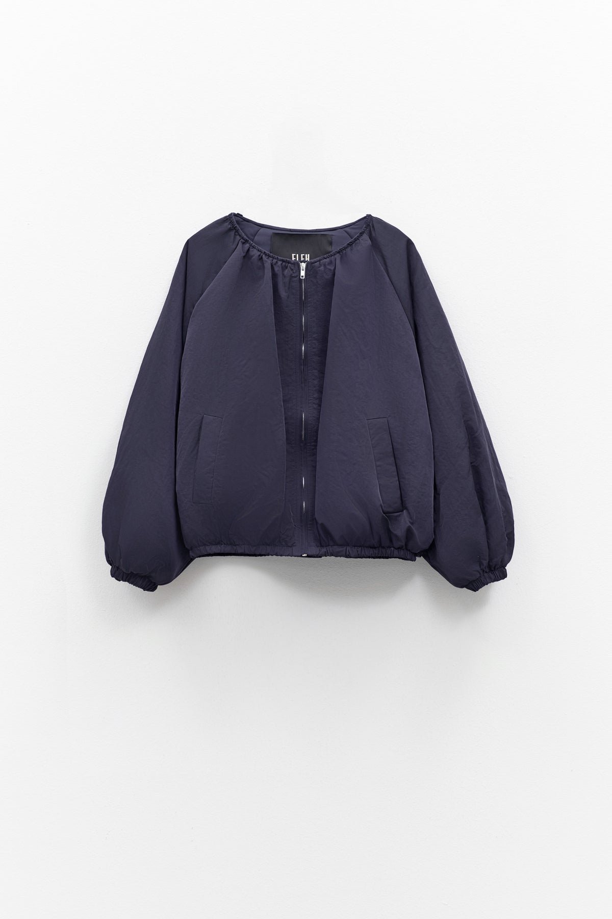 A person models the ELEH NYLON BOMBER JACKET, styled oversized with a matching mini skirt, black ankle boots, and large sunglasses against a plain white background. Brand: ELEH.