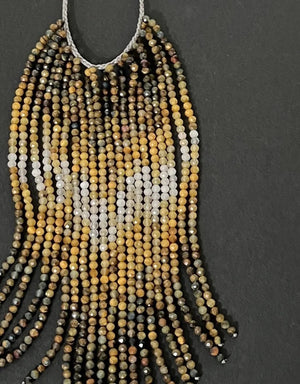 A mannequin wears a textured, curly taupe jacket and the ANN LIGHTFOOT Tiger Eye and Quartz Ombre Cascade Necklace, featuring dramatic dark beaded fringes in a triangular shape. The softly blurred background is neutral.