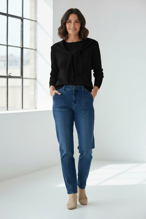 A woman with long brown hair and gold hoop earrings wears blue jeans and a light purple HINSON WU Sloane 3/4 Sleeve Tie Shoulder Cotton Silk Sweater, with a matching sweater draped over her shoulders and tied in front, looking to the side.