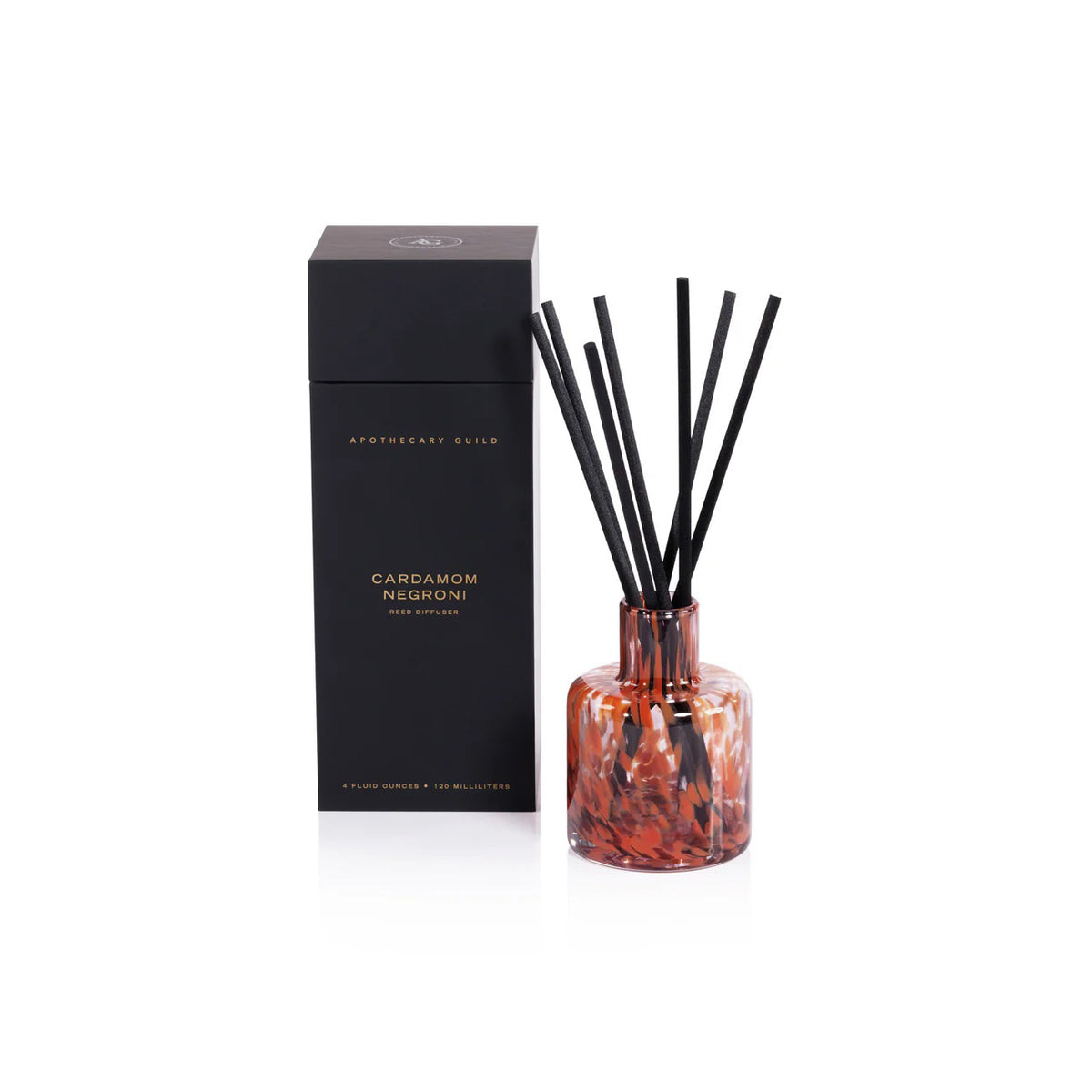 A glass APOTHECARY GUILD OPAL reed diffuser in Cardamom Negroni by ZODAX, with a brown and black marbled design and black reeds, sits beside a tall black box featuring gold text; contains 120 ml of fragrance oil.