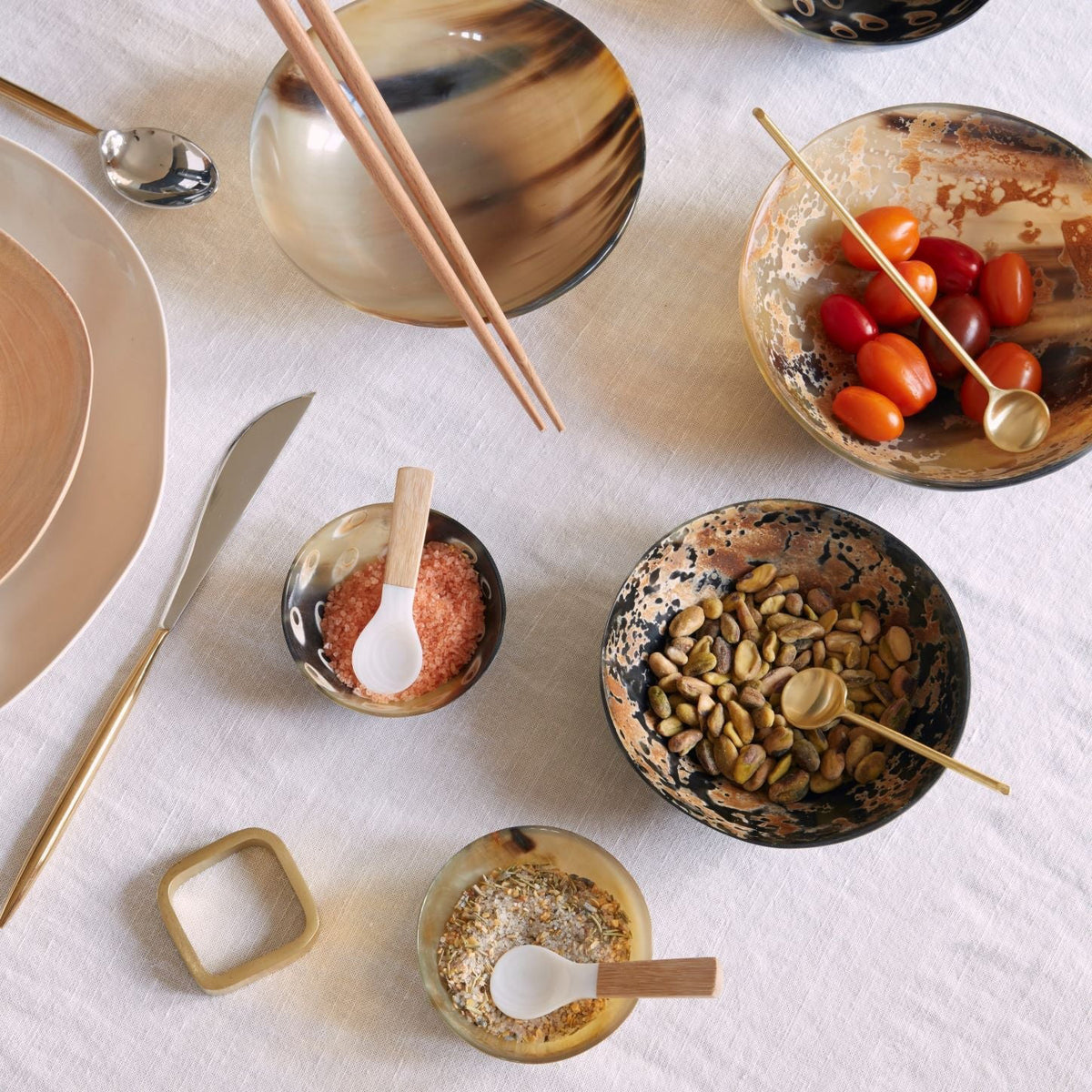 The SPLATTER HORN BOWL SMALL from BE HOME, INC is a small, round bowl made from water buffalo horn, showcasing an intricate marbled pattern in shades of brown, black, and white. Ethically crafted and handmade in Vietnam, the bowl boasts a polished, glossy finish and is set against a vibrant yellow surface.