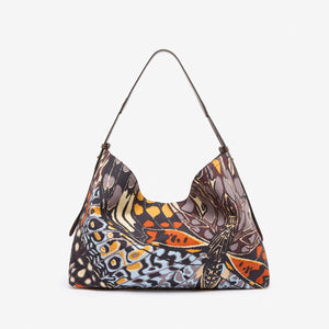 The INOUI EDITIONS MAXI CAMPUS BAG PAPILLON by INOUI is a hobo-style cotton bag with a curved handle, showcasing a vibrant butterfly wing pattern in orange, black, blue, and cream on a plain white background.
