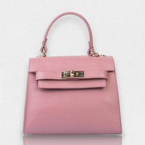 The LE BORSETTE LEATHER SATCHEL BAG is a small, structured satchel-shaped handbag in light pink, featuring a gold clasp at the front. It boasts a single top handle, an adjustable shoulder strap, and two gold-tone hardware pieces on either side of the handle. The textured leather adds to its luxurious and elegant appearance against the plain white background.