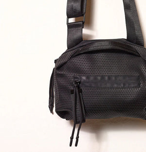 The DANIELLA LEHAVI - BONNIE TRAVEL CROSSBODY features a hexagonal textured pattern, front zipper pocket with two pulls, and an adjustable strap. Crafted from eco-friendly materials, it's shown against a plain light background.