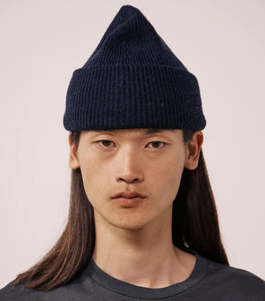The HARTFORD - SEAMLESS WOOL BEANIE IN NAVY by HARTFORD is a dark blue ribbed knit beanie made from 100% wool, featuring a folded brim and shown against a plain light gray background.