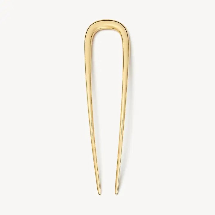 The MACHETE - MIDI FRENCH HAIR PIN IN GOLD by MACHETE is a handcrafted, U-shaped hair accessory with two long, pointed prongs, standing vertically against a plain white background to highlight its elegant simplicity.