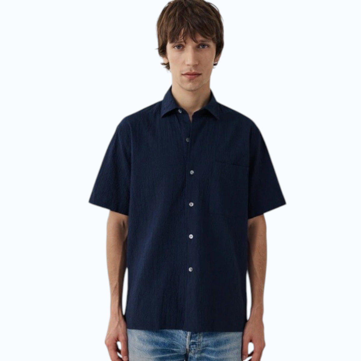 A young man with short brown hair wears the HARTFORD - PEDRO SHIRT IN NAVY and light blue jeans, standing against a plain white background.