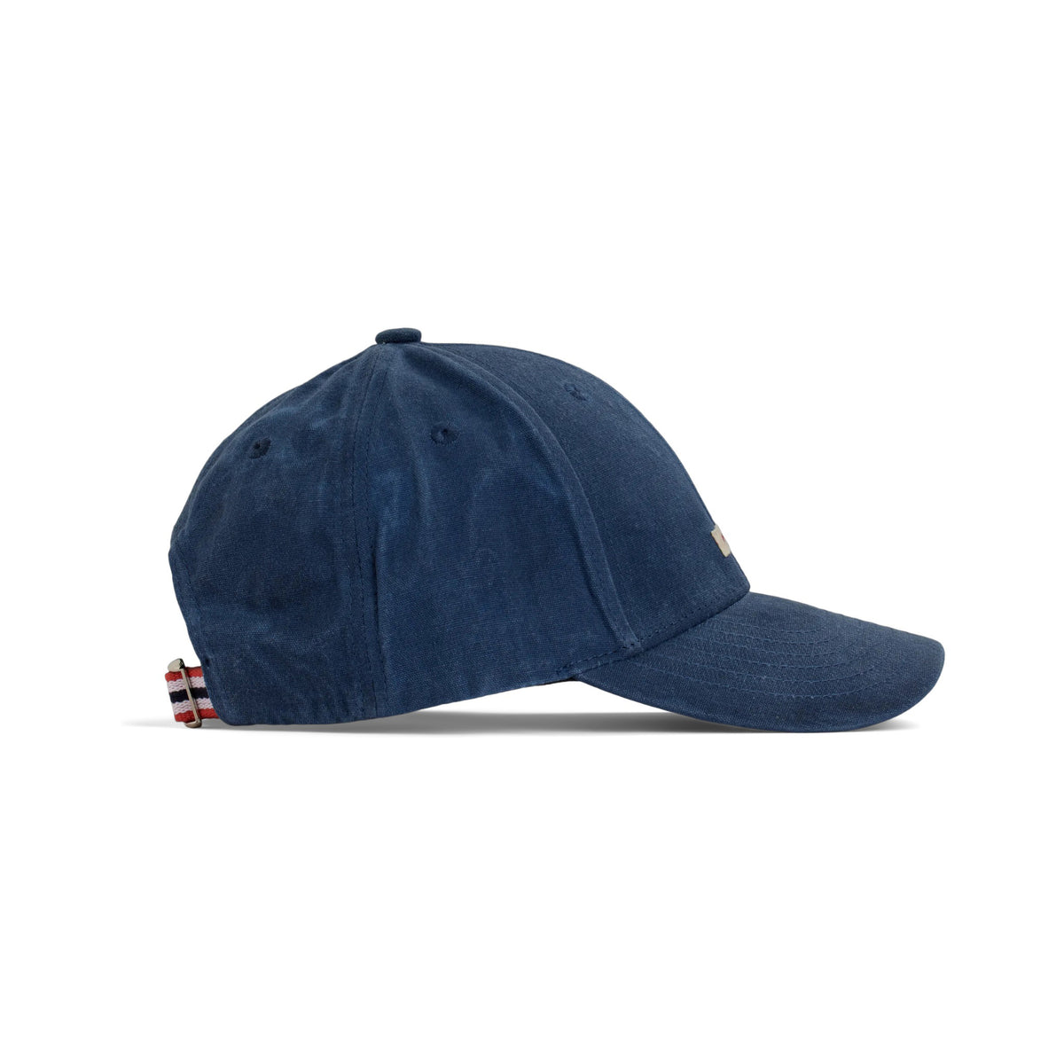 The AMUNDSEN SPORTS - WAXED COTTON CAP in navy blue is shown from the side against a plain white background, featuring a curved brim and an adjustable strap with a red, white, and black checkered norgesreima design.