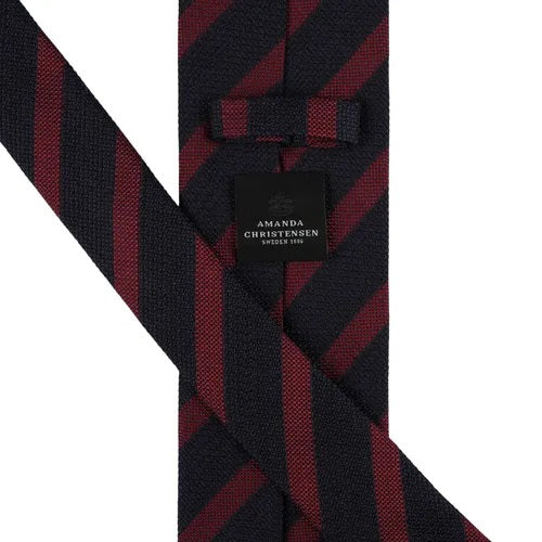 The AMANDA CHRISTENSEN Striped Jacquard Woven Silk Tie in wine red, a men’s formal accessory by AMANDA CHRISTENSEN, features diagonal black and dark red stripes and is displayed rolled up on a white background.