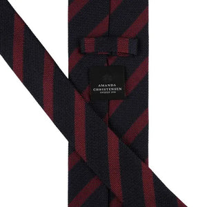 The AMANDA CHRISTENSEN Striped Jacquard Woven Silk Tie in wine red, a men’s formal accessory by AMANDA CHRISTENSEN, features diagonal black and dark red stripes and is displayed rolled up on a white background.