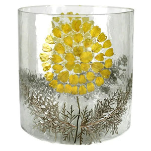 The HOMART ENAMEL HURRICANE WITH YELLOW FLOWER is a cylindrical glass vase featuring pressed yellow petals and green ferns in the design, perfect as a unique garden luminary.