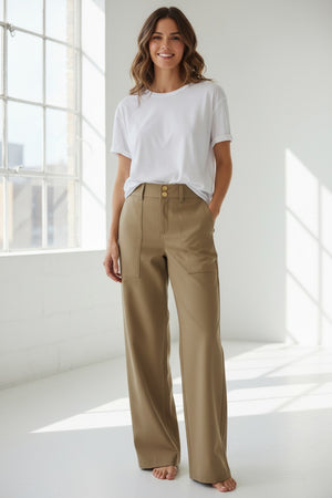 A person is standing against a neutral background with one hand in their pocket, wearing the HINSON WU KELLY Traveler’s Twill Pant in khaki—featuring a high-waisted, wide-leg silhouette, front patch pockets, and a double button closure.