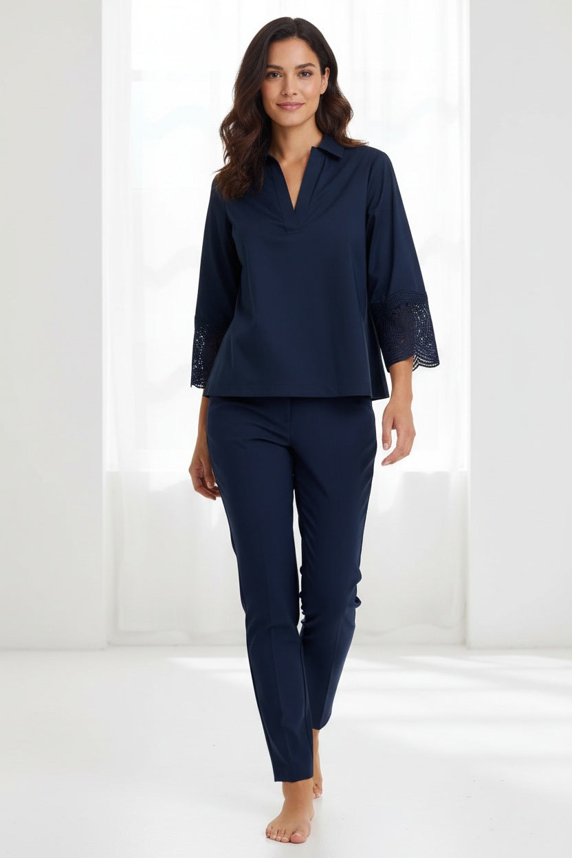 A woman with long red hair wears the HINSON WU MONA Bracelet Sleeve Stretch Polished Cotton Lace Top in navy—a comfortable, stretch cotton blouse featuring three-quarter sleeves with lace accents—paired with navy pants. She accessorizes with blue statement earrings and stands against a plain light background.