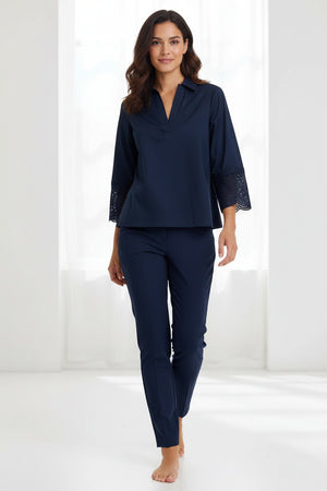 A woman with long red hair wears the HINSON WU MONA Bracelet Sleeve Stretch Polished Cotton Lace Top in navy—a comfortable, stretch cotton blouse featuring three-quarter sleeves with lace accents—paired with navy pants. She accessorizes with blue statement earrings and stands against a plain light background.