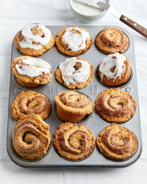 A white pouch labeled "MAISON ZOE FORD - SPEEDY CINNAMON ROLL MIX" features a photo of nine delectable cinnamon rolls, some adorned with a rich glaze, on a baking tray. The 688-gram pouch contains baking mix for making delightful cinnamon roll twists. Text in French is also visible.