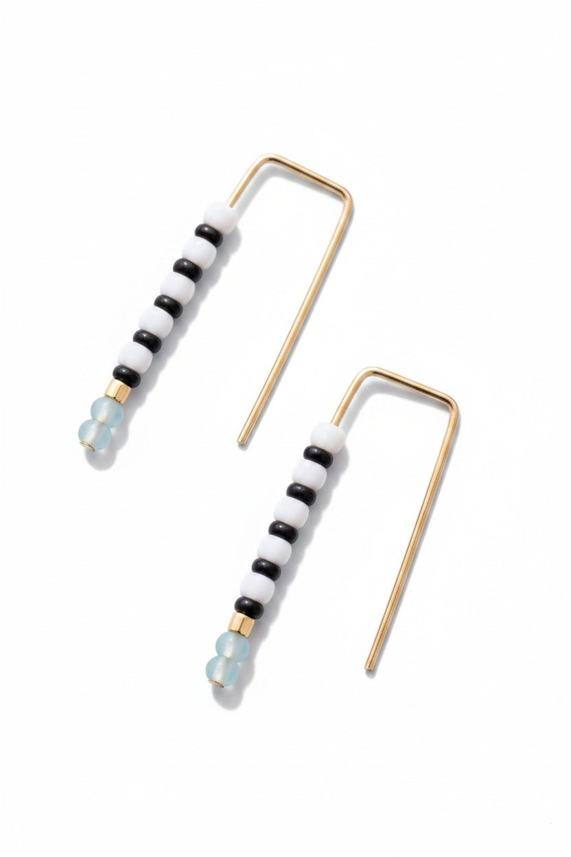 The ALICE RISE - LITTLE QUILL EARRINGS IN TURQUOISE by ALICE RISE, featuring minimalist 14k gold filled design and turquoise beads, are displayed on a textured light blue background—perfect for handmade jewelry lovers.