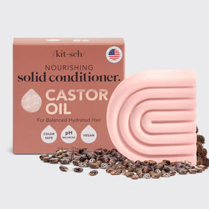 A pink KITSCH - CASTOR OIL NOURISHING CONDITIONER BAR and its box are shown with castor beans. The box notes it's color safe, pH balanced, vegan, and designed to nourish dry hair while controlling frizz.