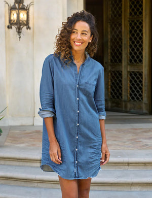 The FRANK & EILEEN Mary Ruffle Shirtdress in vintage stone-washed indigo features long sleeves rolled up to the elbows, a ruffle collar, and a front button-down design with a chest pocket. A slightly frayed hem adds charm against the plain white background.