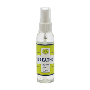A small green plant in a face-shaped pot sits next to a large jar labeled "BAUDELAIRE - BREATHE SHOWER MIST." Above, smaller bottles of eucalyptus essential oil and a wooden brush rest on a white shelf with a gray geometric background, creating an inviting space for your aromatherapy steam room.